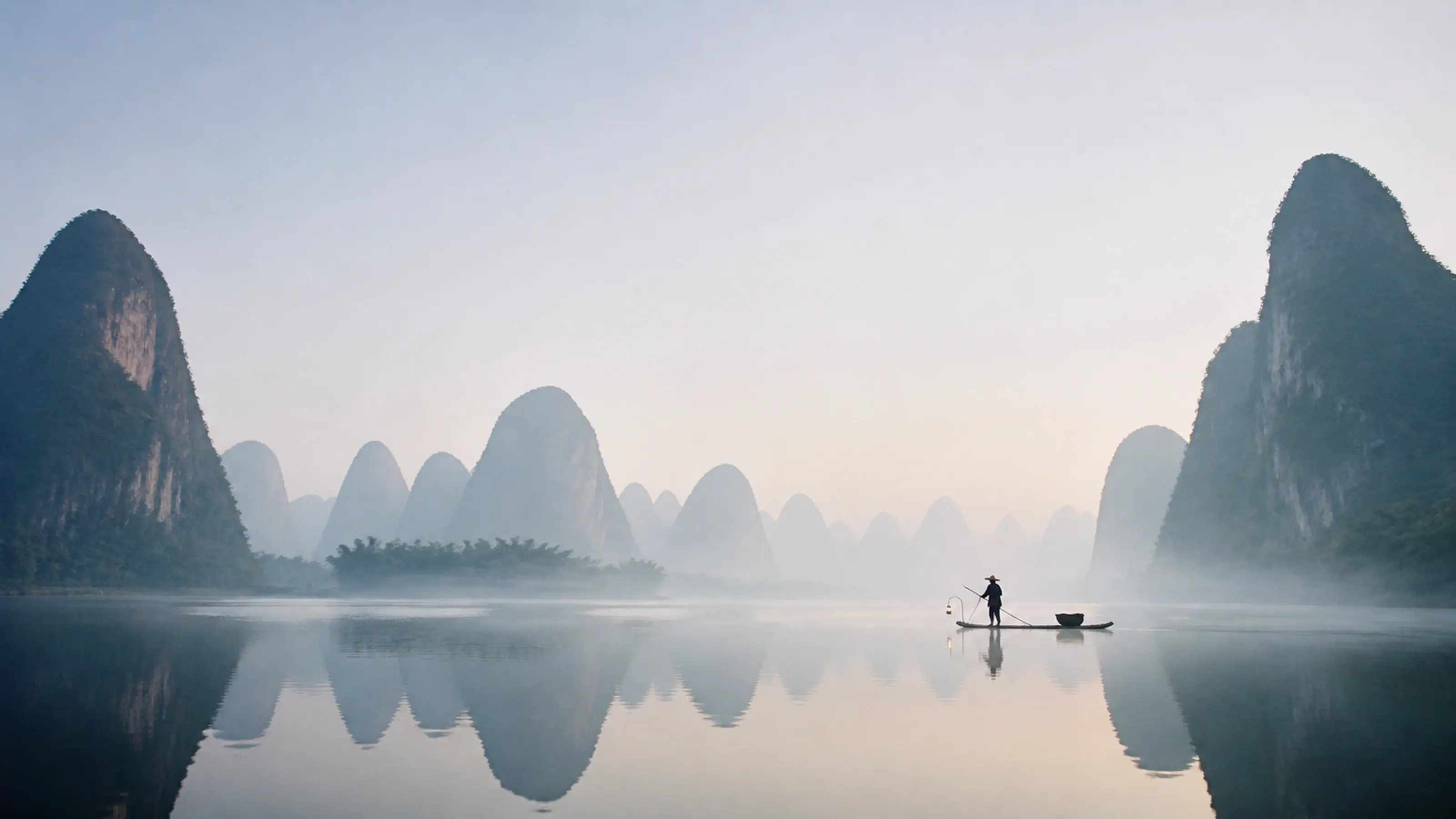 Dawn on the Li River: karst peaks in silver mist and a lone cormorant fisherman with a lamp