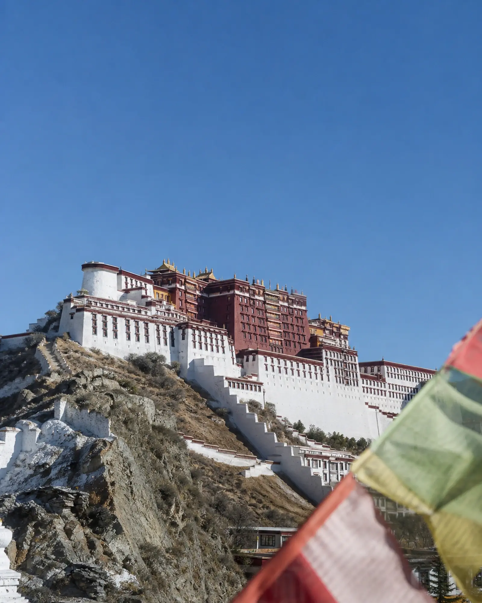 The Potala Palace rising in thin bright morning light, prayer flags in the foreground